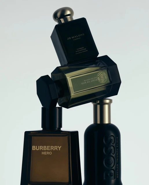 Four perfume bottles, including Burberry Hero, Jo Malone London, and Hugo Boss, stacked in front of a plain white studio background.