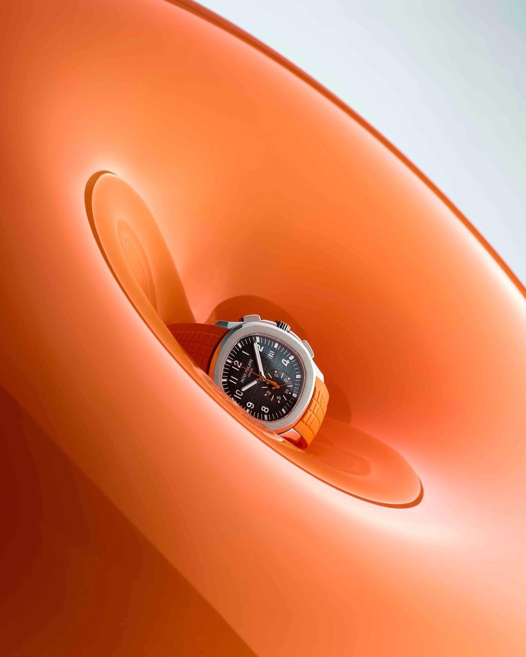Silver and orange wristwatch showcased inside a glossy orange circular structure, close-up studio shot.