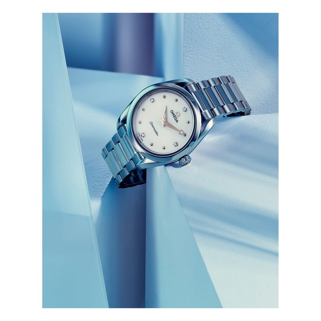 Elegant silver Omega Constellation watch with a white dial and diamond markers, set against an abstract blue and white background.