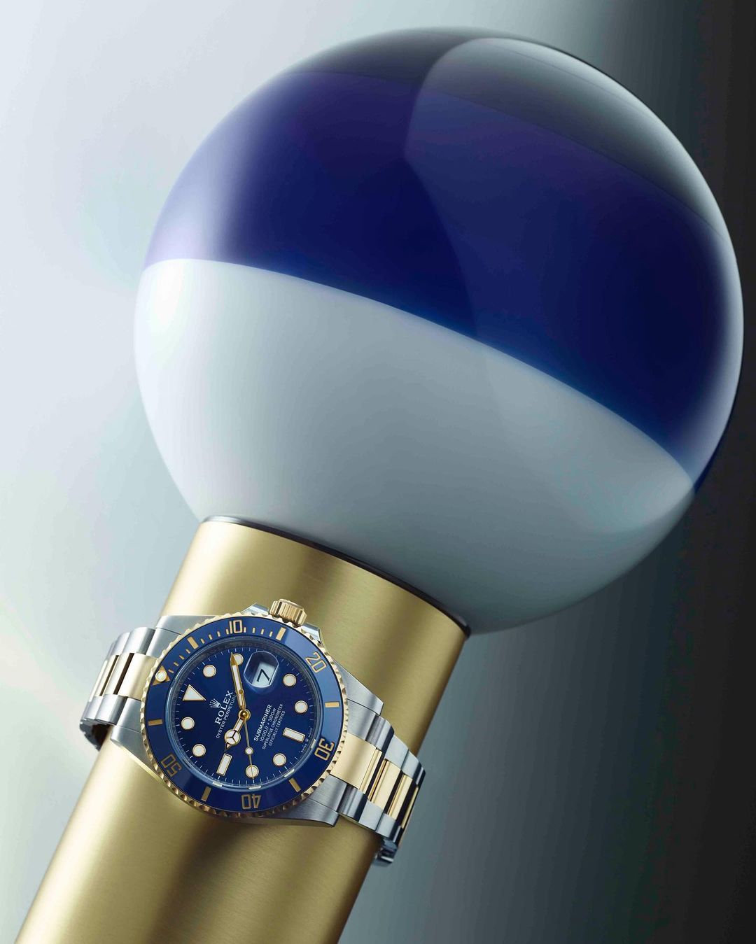 Luxury wristwatch on a gold display stand with a white and blue sphere backdrop, showcasing elegant design and precision craftsmanship.