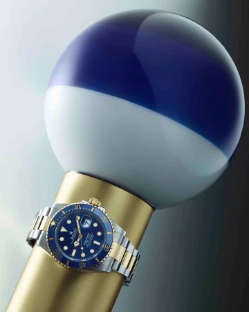 Luxury wristwatch on a gold display stand with a white and blue sphere backdrop, showcasing elegant design and precision craftsmanship.
