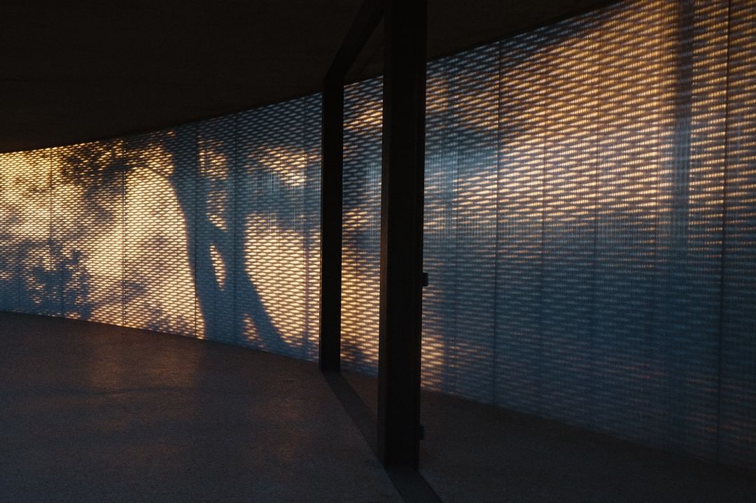 Abstract view of a room interior featuring a curved wall with patterned light and shadow, creating a textured, illuminated architectural space.