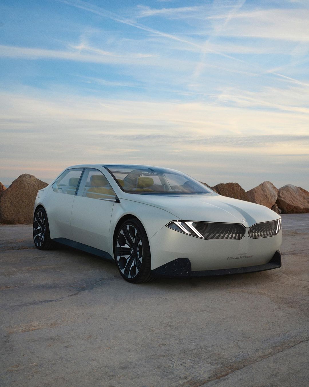 Sleek white BMW concept car parked on a concrete surface with a scenic view of a blue sky and rocky hills in the background.