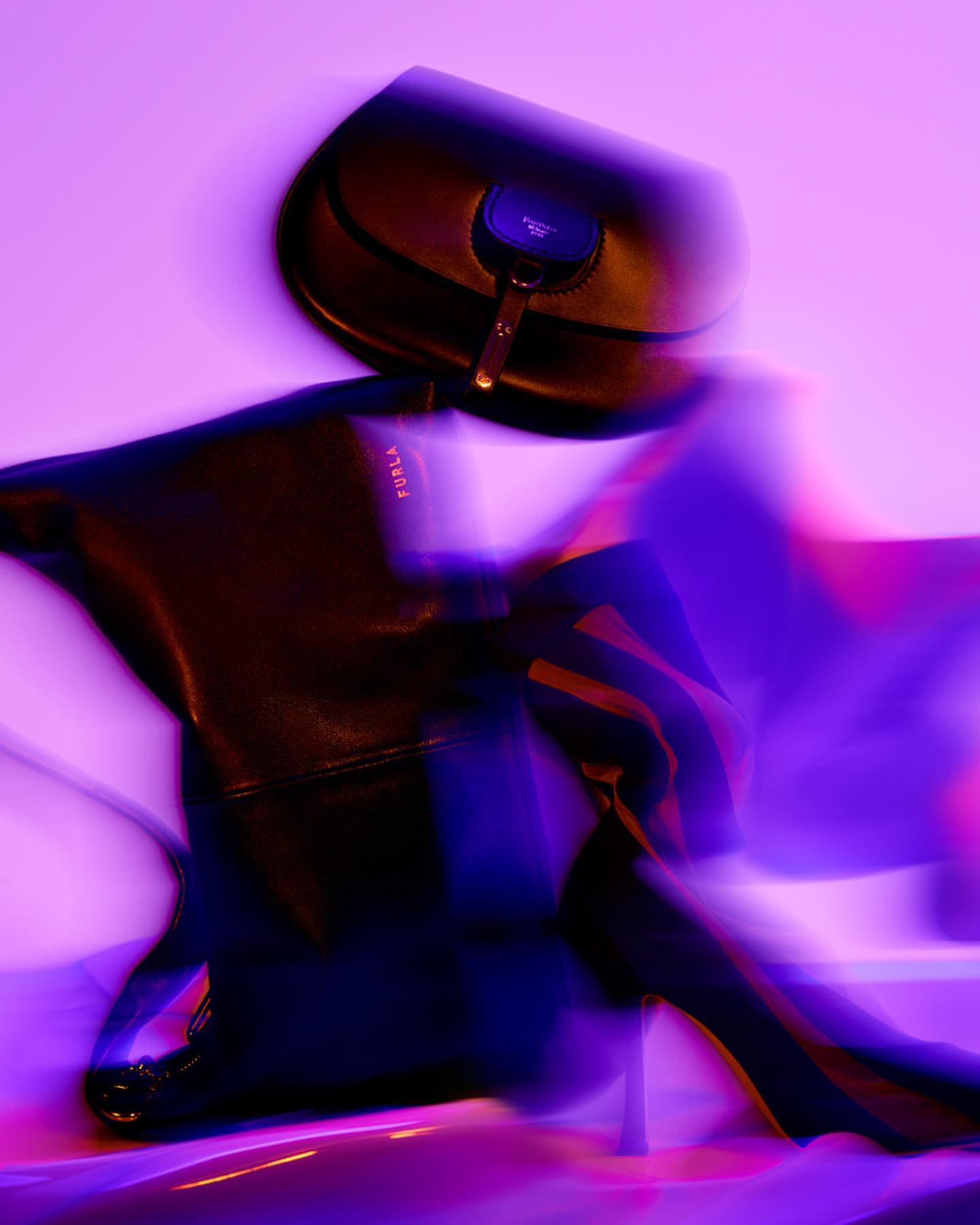 Fashion still life with black leather purse and high heel boot. Dark and elegant composition. Studio lighting with purple hue.