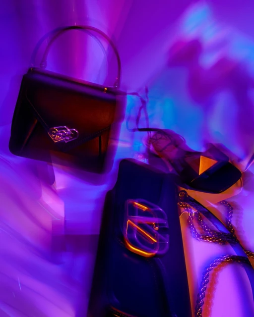 Fashion photography featuring a black handbag and purse illuminated by vibrant purple and blue lighting against an abstract backdrop.