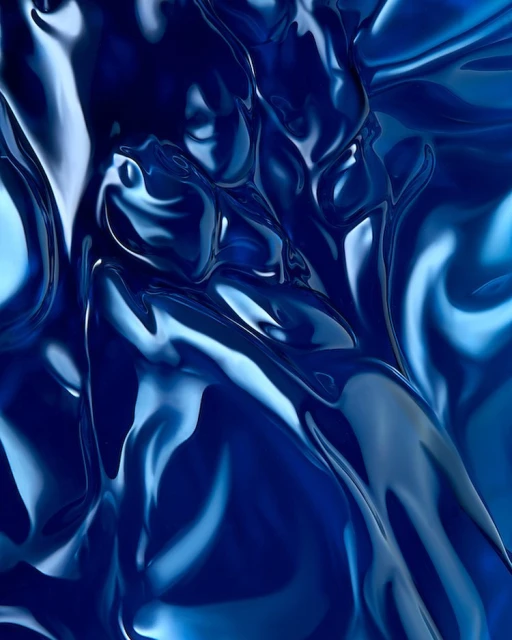 Abstract image of draped, shiny blue fabric with flowing forms and highlights, creating a dynamic and elegant visual texture.