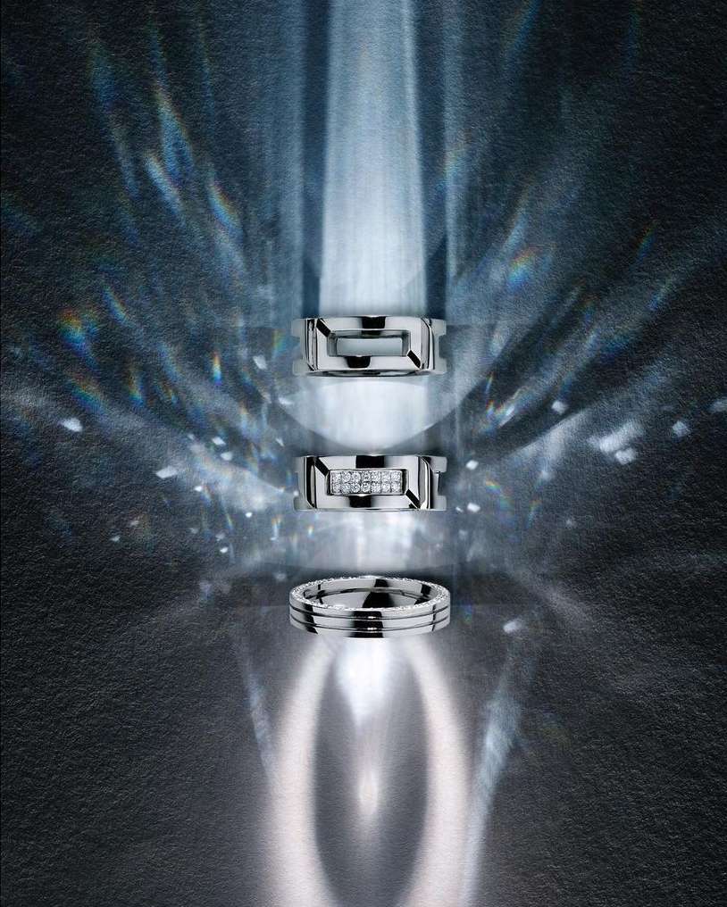 Three silver metal rings with diamond accents are displayed against a textured gray backdrop with soft, blurred light patterns.