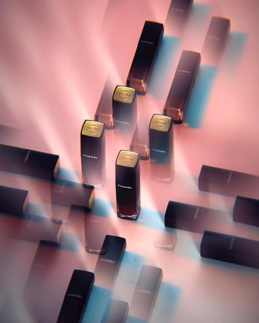 Several black and gold Chanel lipstick tubes are displayed on a pink and light blue gradient background with soft, diffused lighting.