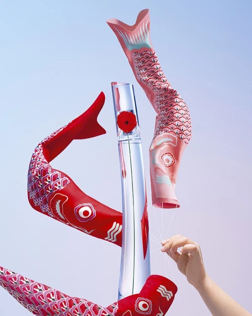 Still-life shot of red and pink carp streamers and a glass vase holding a red flower. A hand with strings is visible.