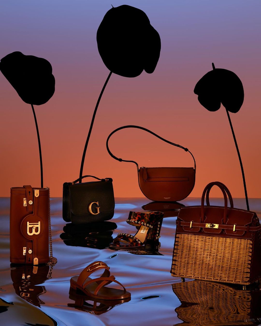 Fashion still life featuring several luxury handbags and sandal pairs arranged on a reflective surface, set against a gradient background.