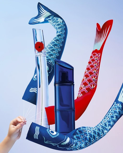 Still life shot of perfume bottles surrounded by colorful koinobori (Japanese carp streamers) against a graduated blue background.