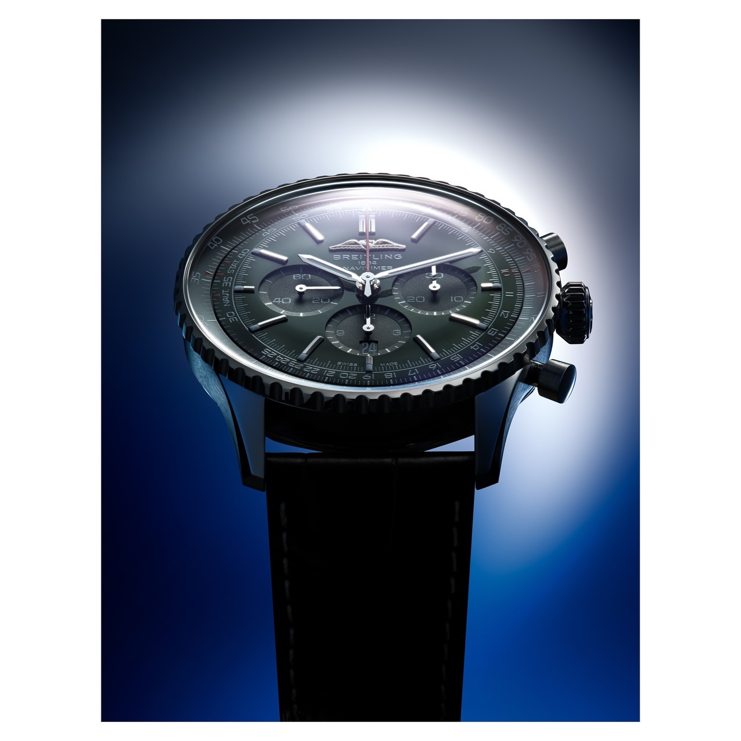 Elegant dark-faced chronograph watch with a black leather strap, captured in a professional studio product shot with moody blue lighting.