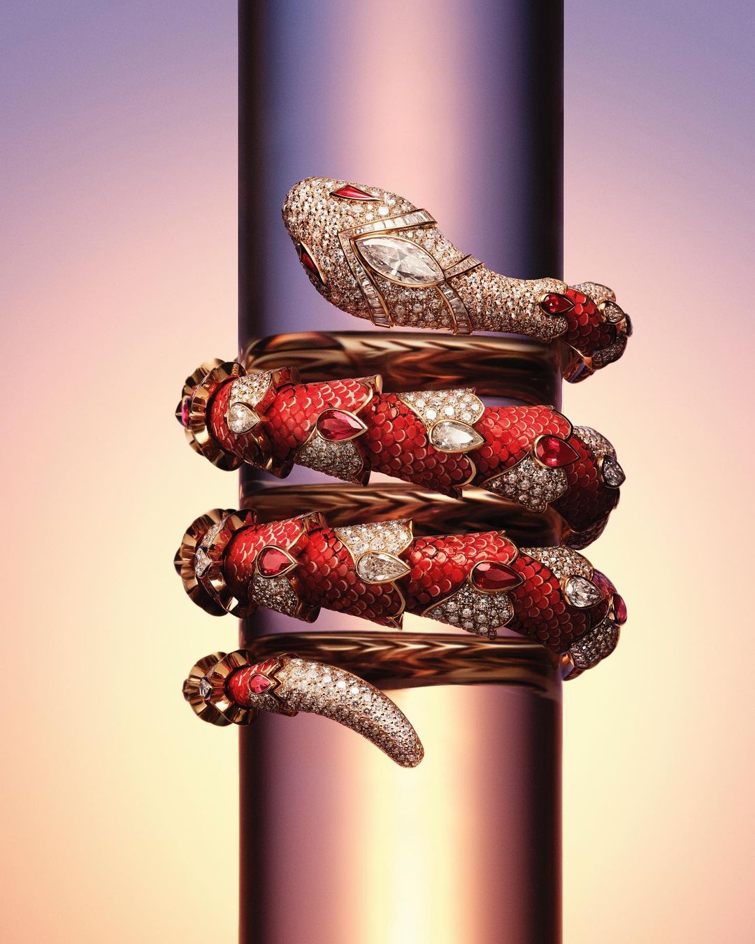Close-up of a snake-shaped bracelet made of gold, diamonds, and rubies wrapped around a reflective cylindrical surface.