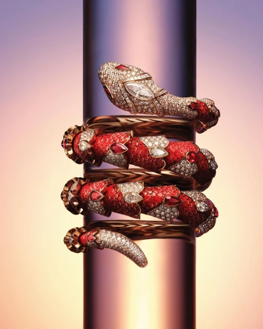 Close-up of a snake-shaped bracelet made of gold, diamonds, and rubies wrapped around a reflective cylindrical surface.