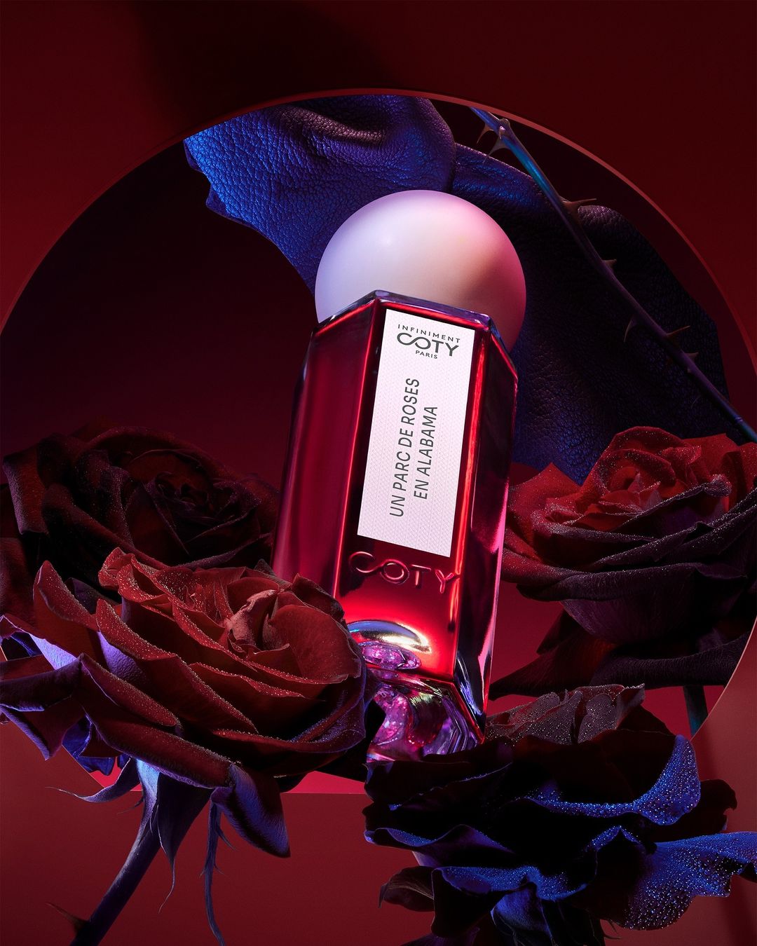 Elegant Coty perfume bottle with a spherical cap and floral accents, presented in a studio setting with moody lighting and a red color palette.
