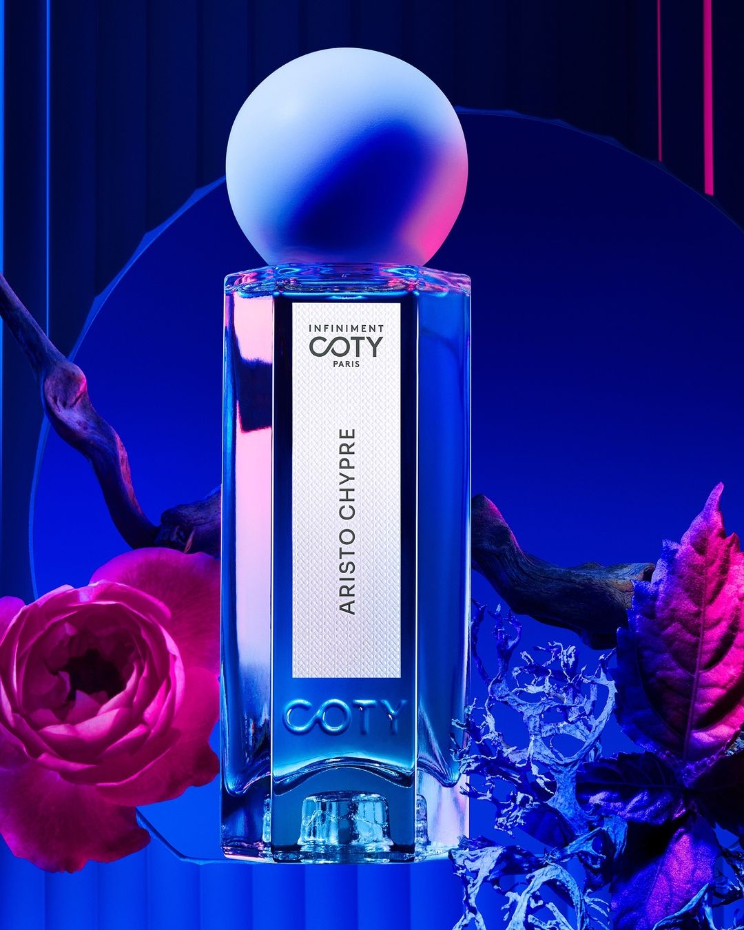 Striking product shot featuring a Coty perfume bottle with a spherical cap, accented by floral elements and dramatic blue and pink lighting.