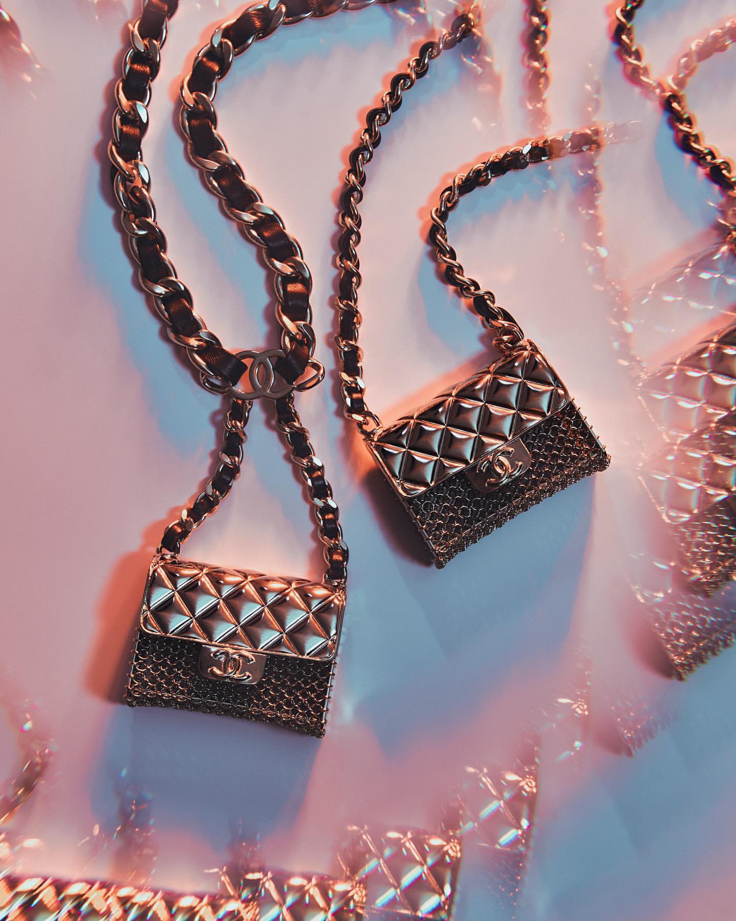 Several small, quilted gold purses with chain straps are displayed on a light pink surface with soft, diffused studio lighting.