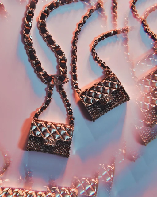 Several small, quilted gold purses with chain straps are displayed on a light pink surface with soft, diffused studio lighting.