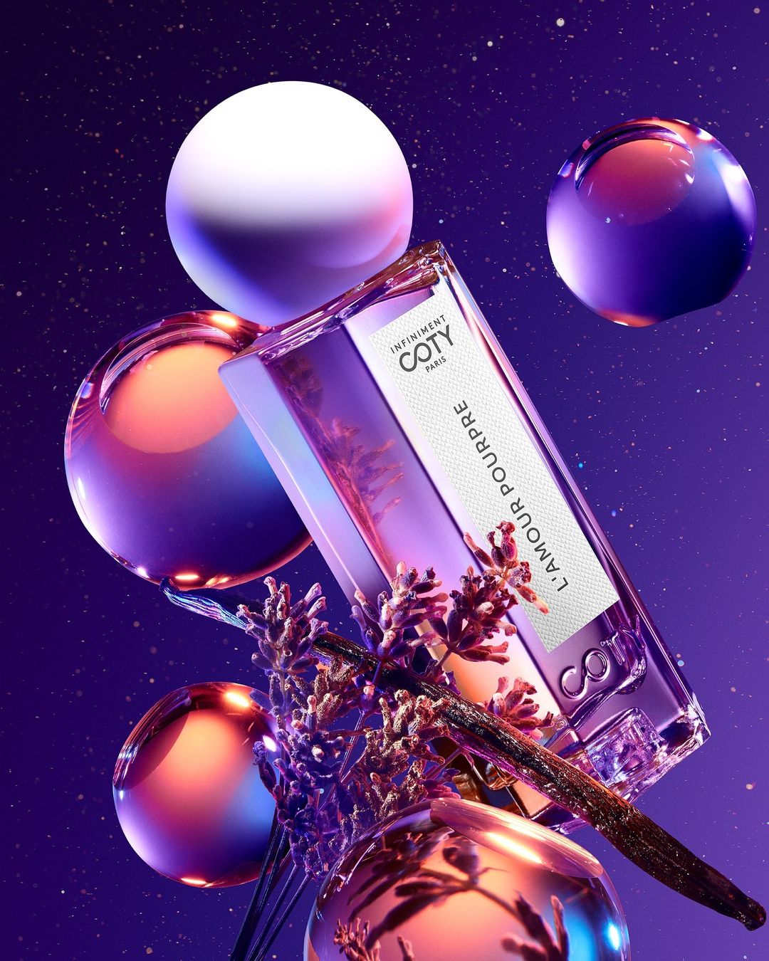Coty L'Amour Pourpre perfume bottle floats against a purple starry background with lavender and spheres, product photography in a studio.