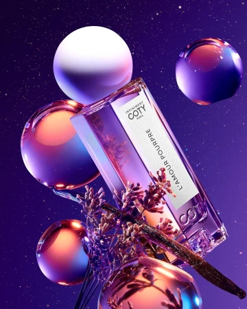 Coty L'Amour Pourpre perfume bottle floats against a purple starry background with lavender and spheres, product photography in a studio.