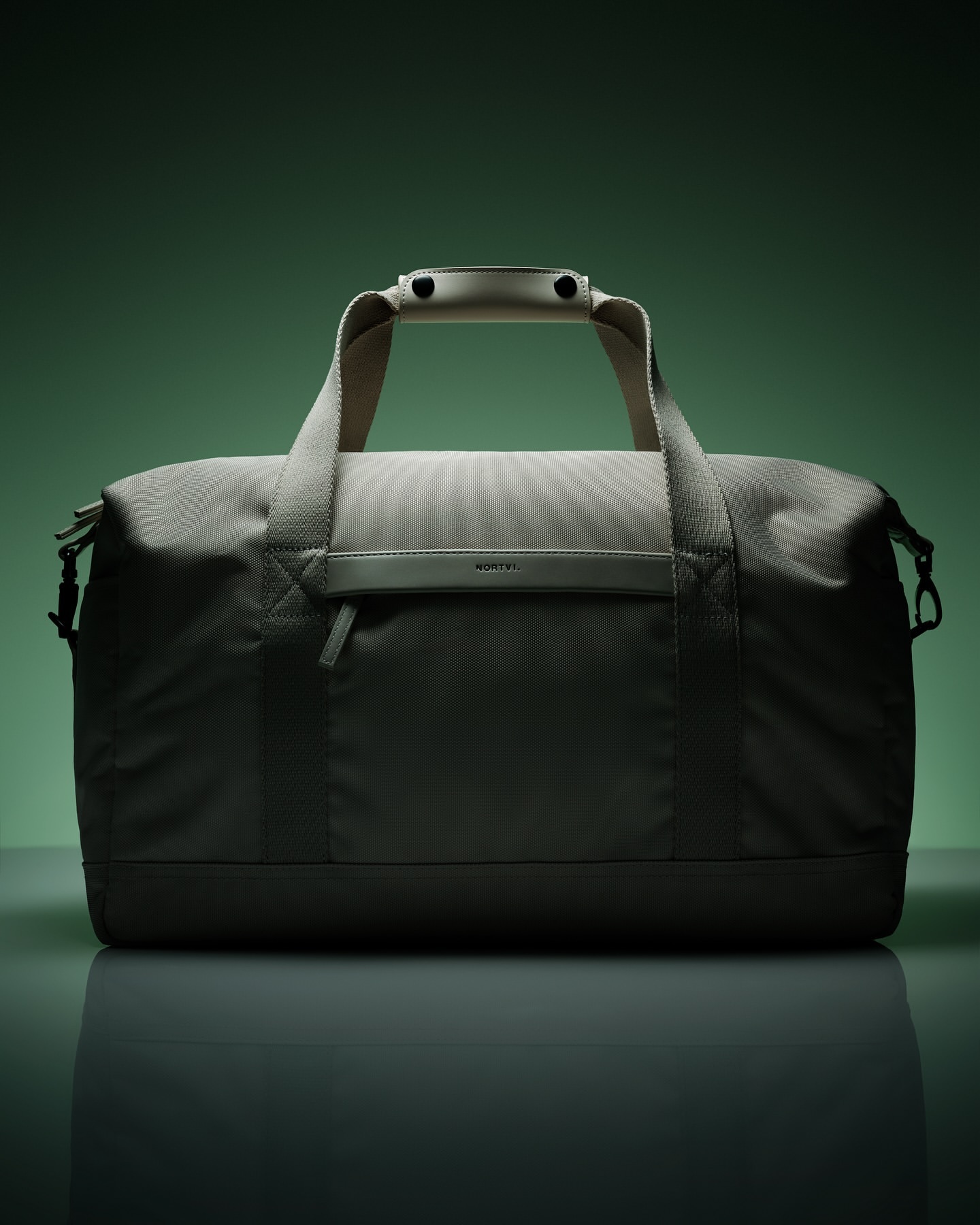 Studio shot of a gray duffel bag featuring a textured design, handle, and front pocket, set against a green backdrop with studio lighting.