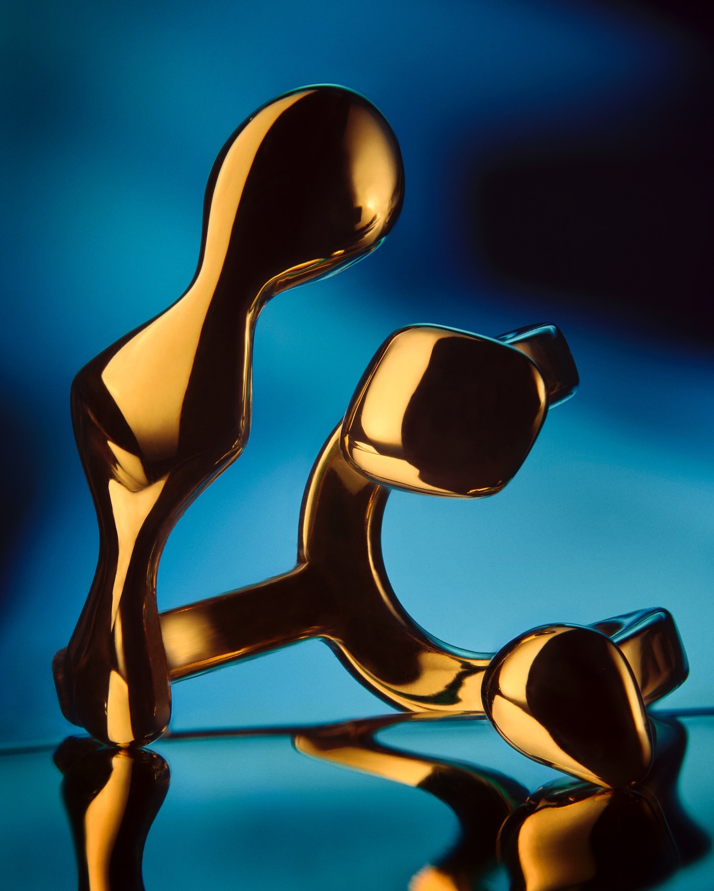 Abstract golden sculpture on a reflective surface against a gradient blue background, showcasing modern art and design elements.