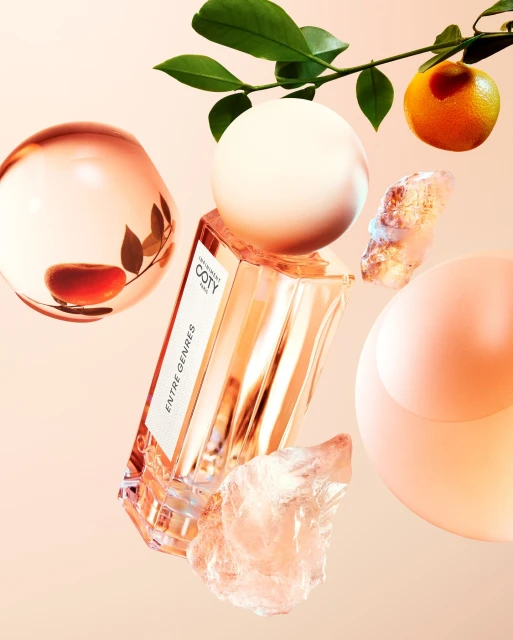 Perfume bottle with geometric shapes, orange, and leaves on a soft pink background for a beauty or fragrance advertisement.