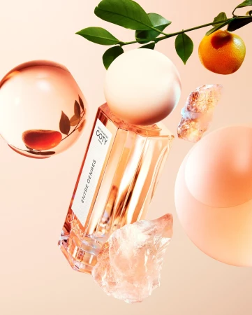 Perfume bottle with geometric shapes, orange, and leaves on a soft pink background for a beauty or fragrance advertisement.
