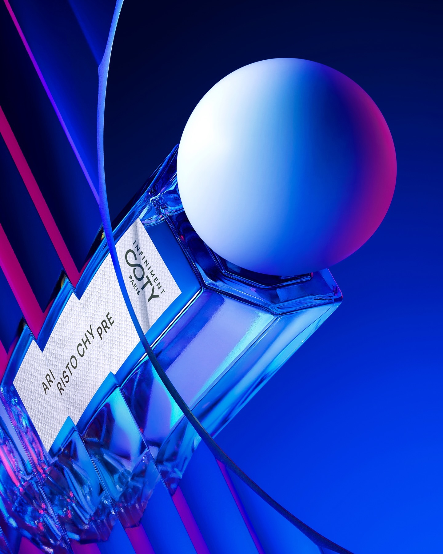 Geometric bottle of COTY fragrance with a spherical cap set against a vibrant blue and pink background. Product photography.