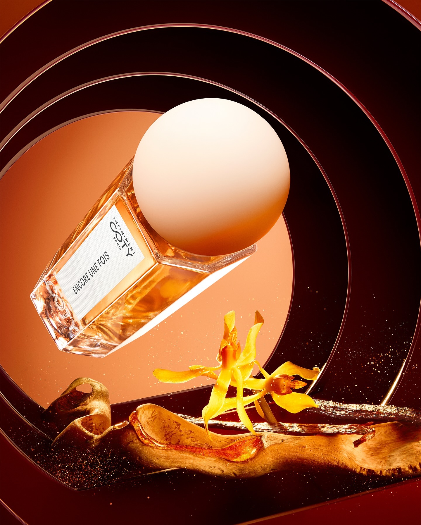 Still life shot of a Coty perfume bottle with a spherical cap, an orchid, and brown resin swirls against a spiral backdrop.