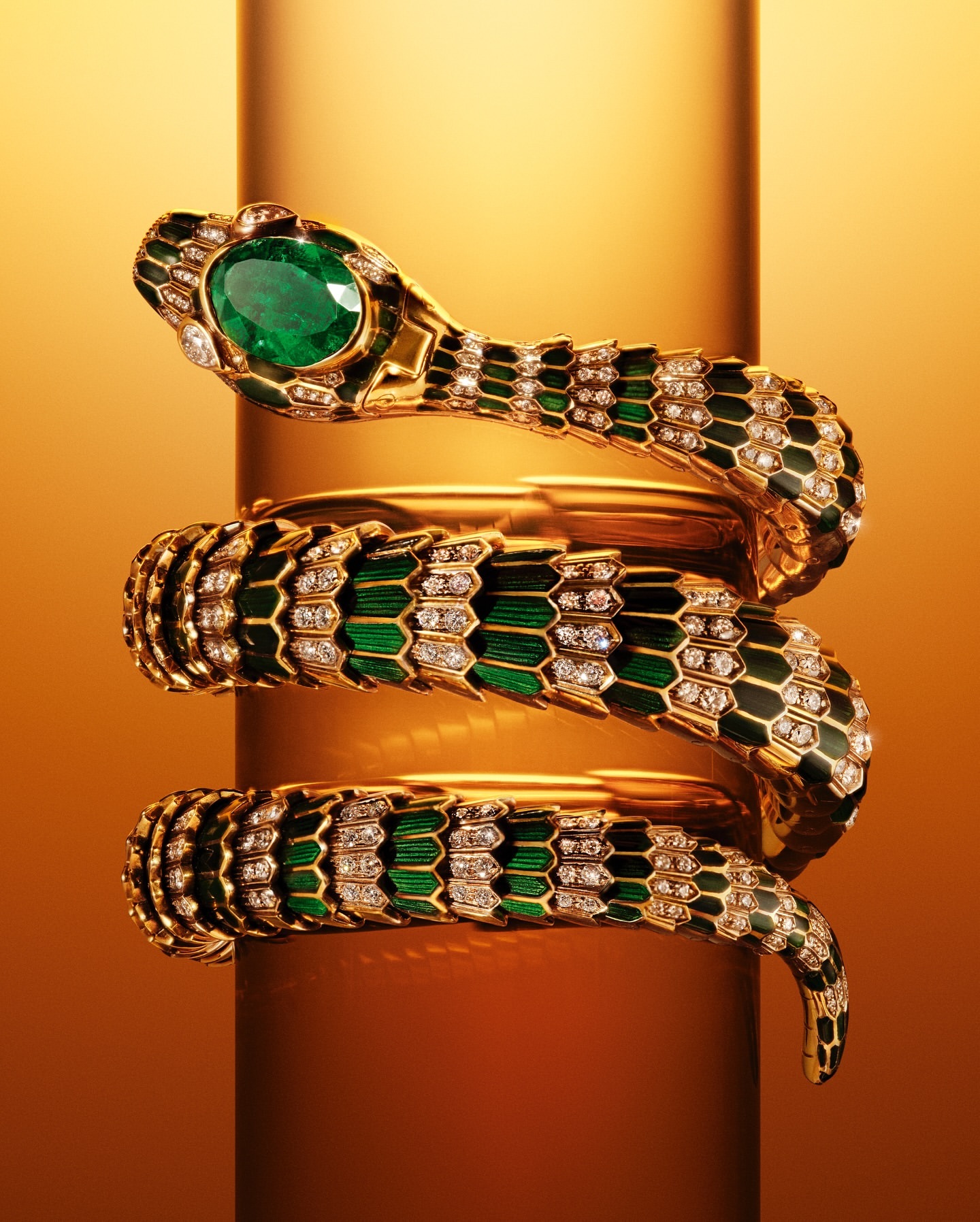 Elegant snake bracelet in gold and green with a large emerald on a reflective gold stand. Jewelry concept for fashion and beauty.