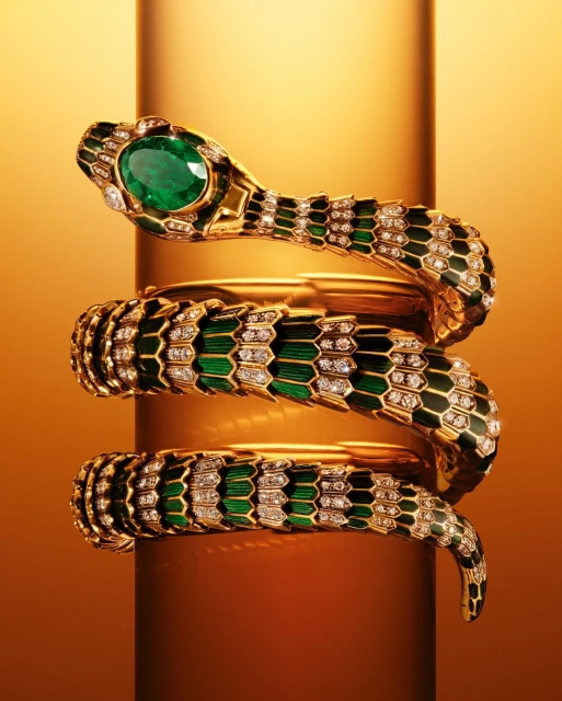 Elegant snake bracelet in gold and green with a large emerald on a reflective gold stand. Jewelry concept for fashion and beauty.