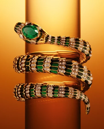 Elegant snake bracelet in gold and green with a large emerald on a reflective gold stand. Jewelry concept for fashion and beauty.