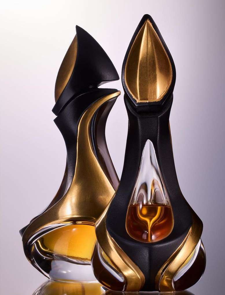 Two uniquely shaped decorative bottles, one containing a yellow liquid, featuring black and gold accents, set against a gradient background.