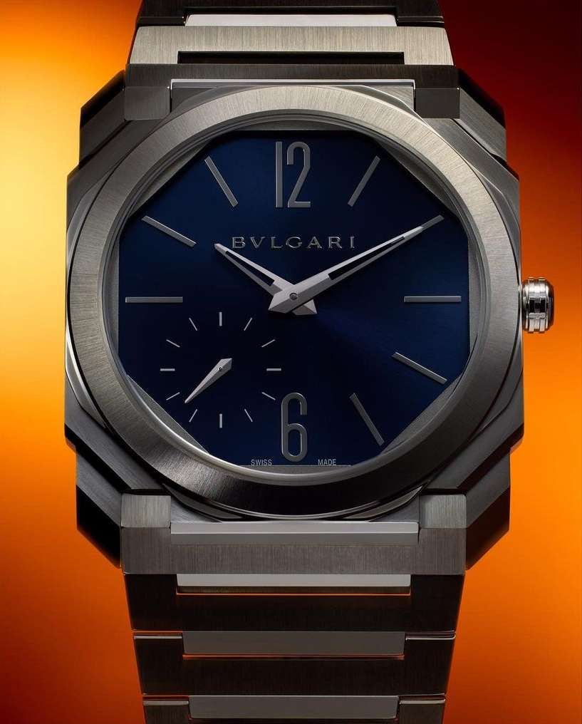 Close-up studio shot of a luxury wristwatch with an octagonal case, blue dial, silver hands, and a stainless steel link bracelet.