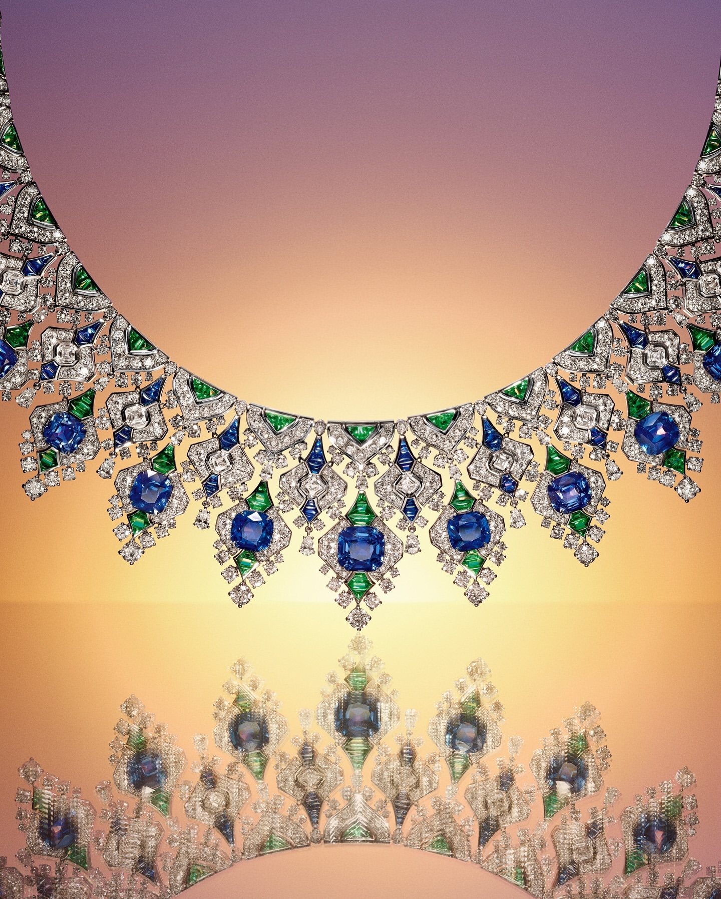 Elegant jewellery product shot featuring an ornate diamond necklace with blue and green gemstones against a gradient light-colored background.