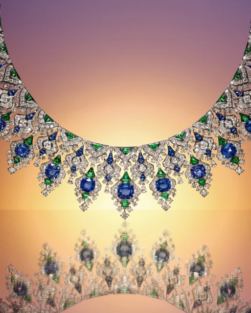 Elegant jewellery product shot featuring an ornate diamond necklace with blue and green gemstones against a gradient light-colored background.