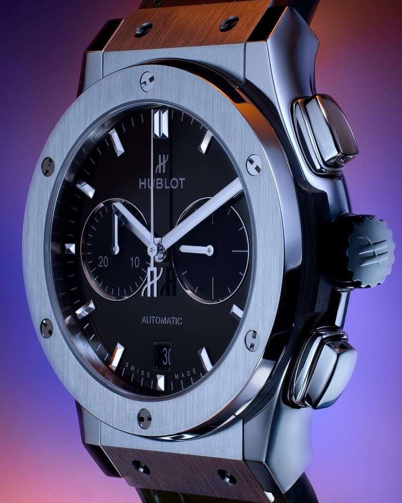 Close-up of a stainless steel Hublot watch with a black dial, silver hands, and an automatic movement display, showcasing luxury timekeeping.