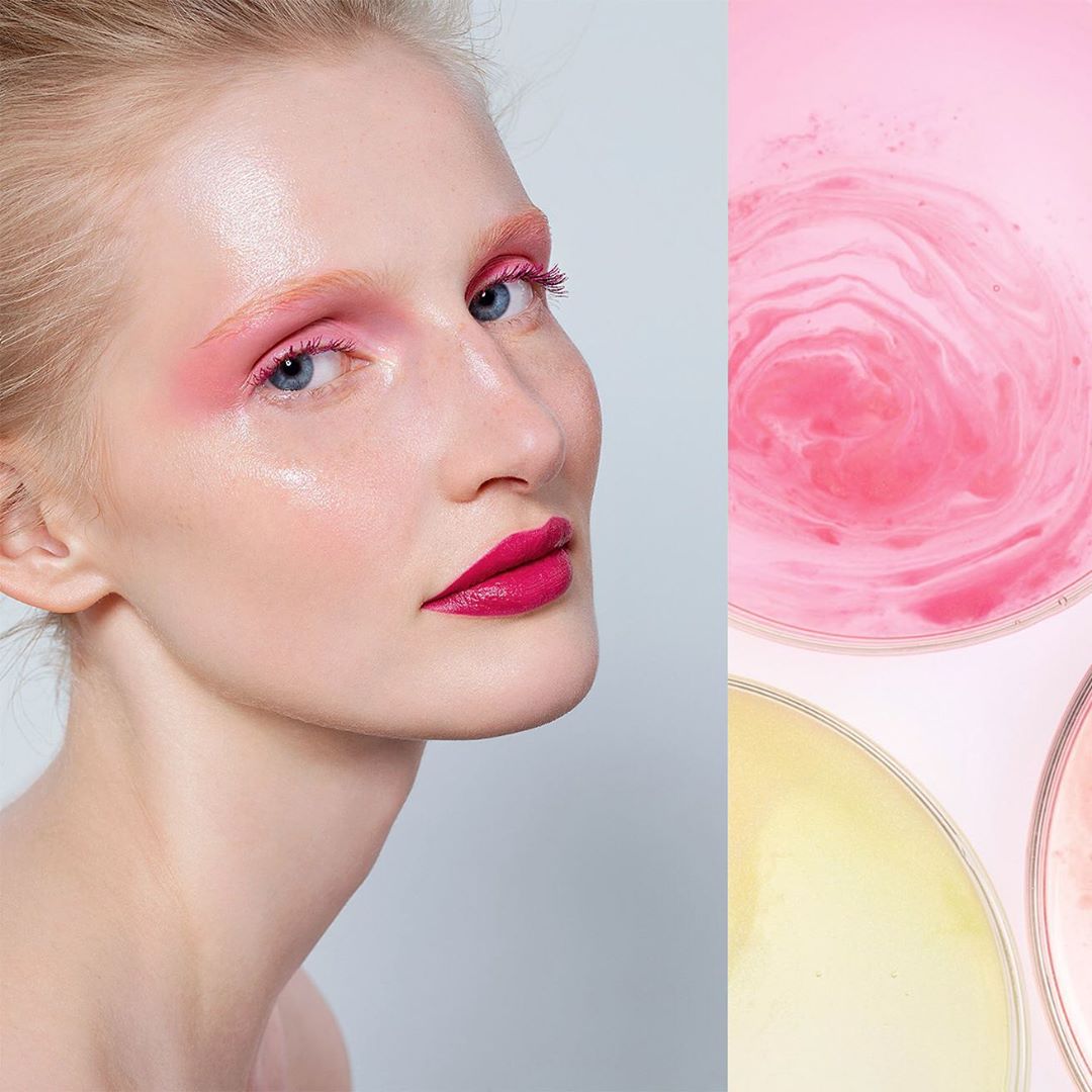 Close-up beauty shot of a blonde woman with pink makeup, juxtaposed against pink and yellow liquid in circular dishes, studio lighting.