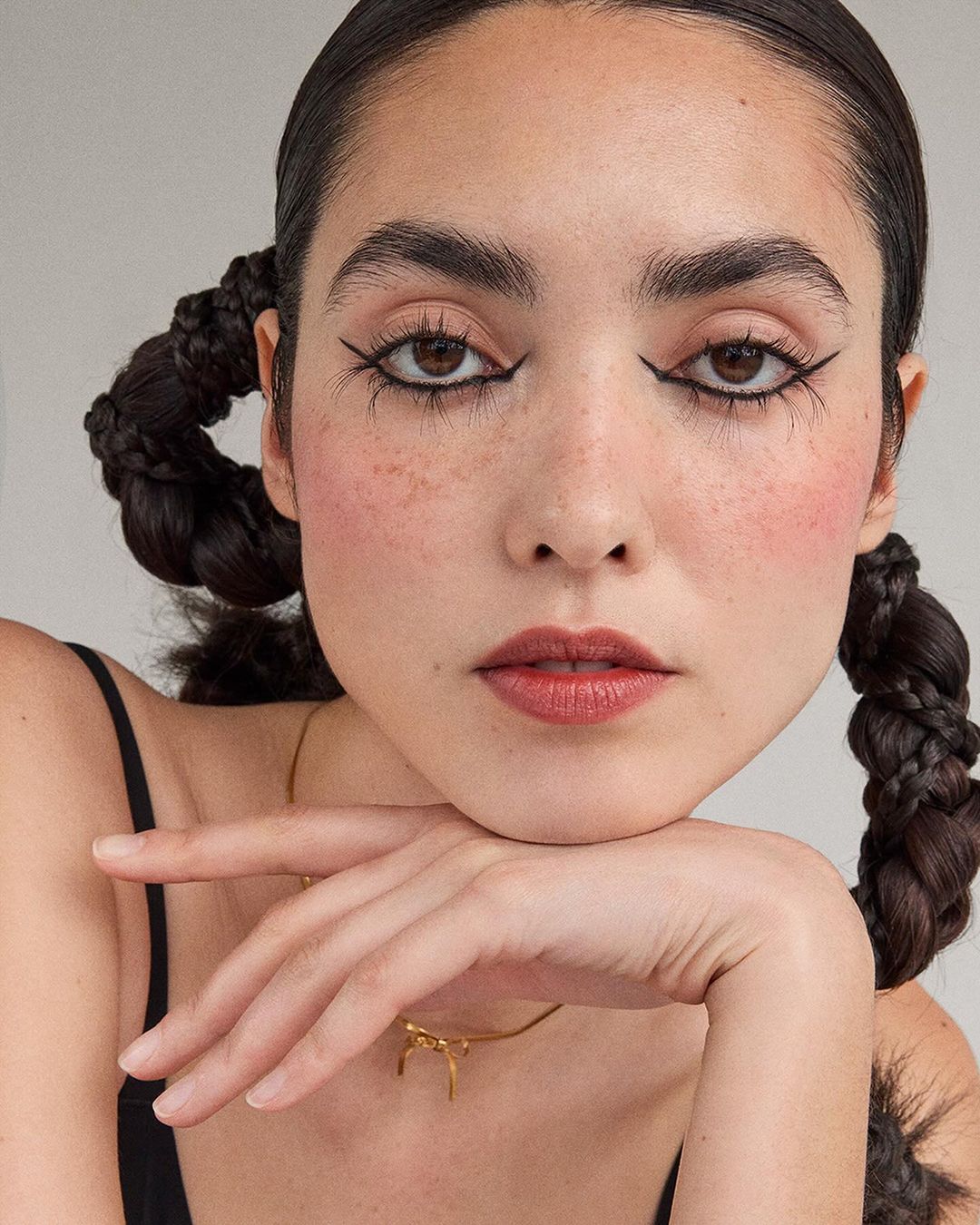 Close-up portrait of a woman with pigtails, dramatic eyeliner, and red blush posing with her chin resting on her hand.