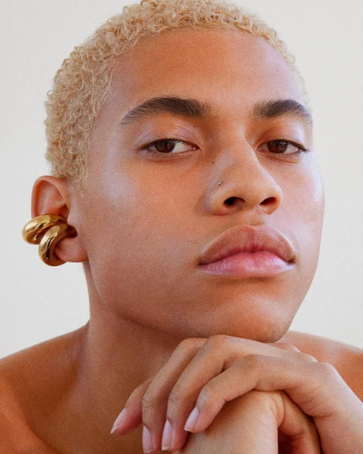 Close-up portrait of a young adult with fair skin, blonde hair, and striking gold ear cuffs, creating a bold fashion statement.