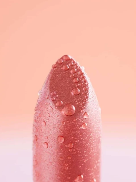 Close-up of a pink lipstick with water droplets on the surface. Beauty shot with a peach-colored background for cosmetic advertising.