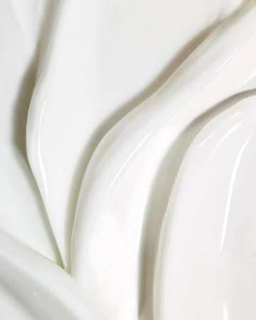 Close-up view of textured white cream with glossy ridges and smooth surface, highlighting purity and rich moisturization.
