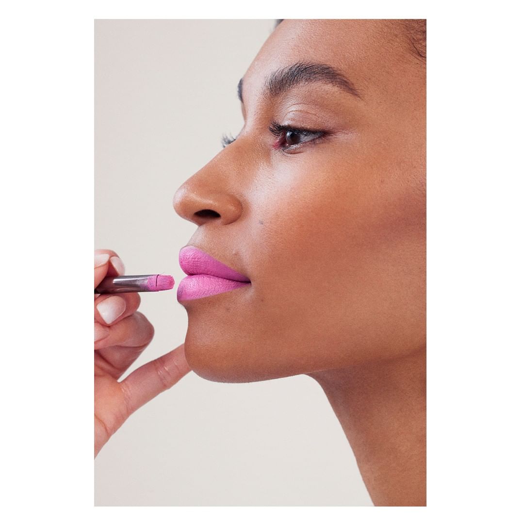 Close-up of a model having bright pink lipstick applied with a silver lipstick applicator in a beauty or fashion context.