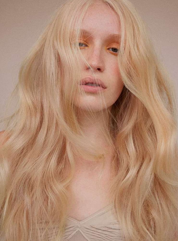 Close-up portrait of a fair-skinned woman with long, wavy blonde hair and subtle yellow eyeshadow, shot by Barbara Donninelli.