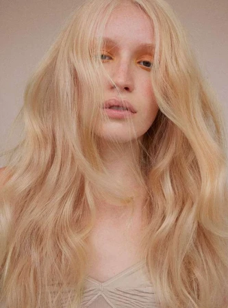 Close-up portrait of a fair-skinned woman with long, wavy blonde hair and subtle yellow eyeshadow, shot by Barbara Donninelli.