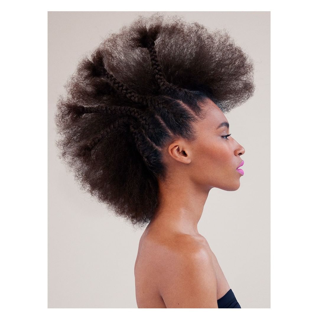 Profile portrait of Black woman with afro hairstyle featuring braids, wearing strapless top in a studio with soft, neutral lighting.