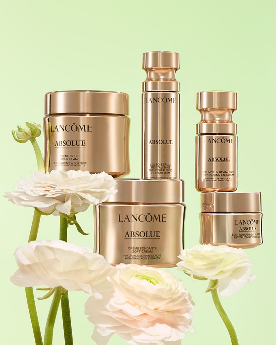 Lancôme Absolue skincare product line displayed with white flowers against a light green backdrop in a beauty advertisement.