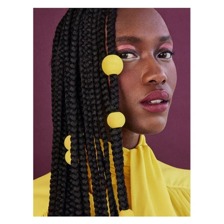Close-up portrait of a Black woman with long black box braids decorated with bright yellow spherical beads, wearing a yellow high-neck blouse.