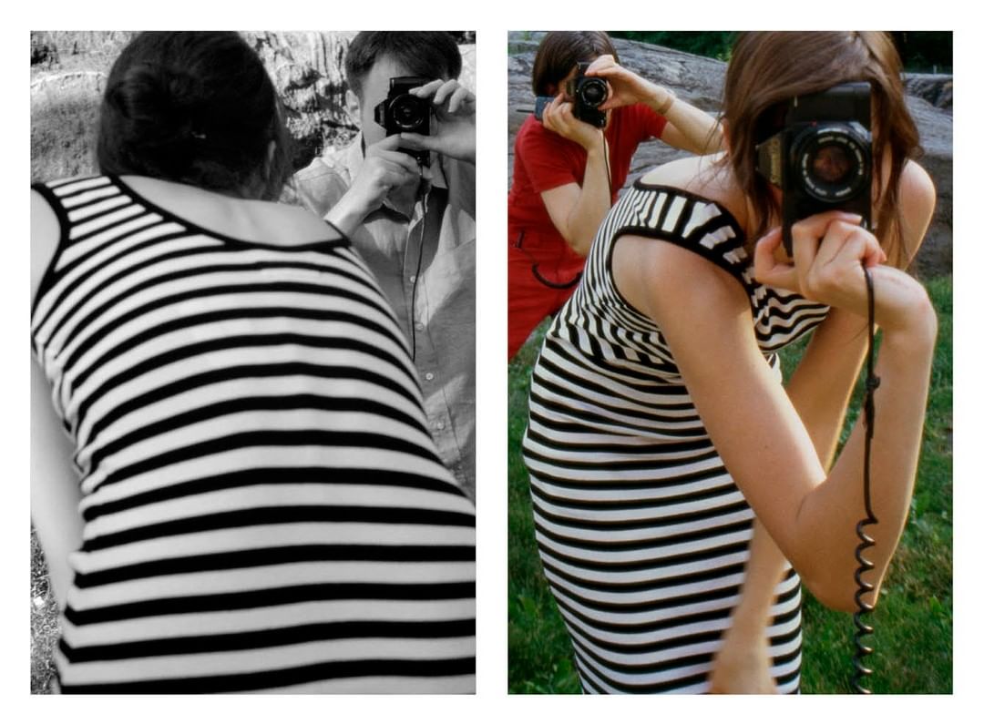 Two women wearing striped dresses photograph each other with vintage cameras outdoors in grassy area, split between color and black-and-white.